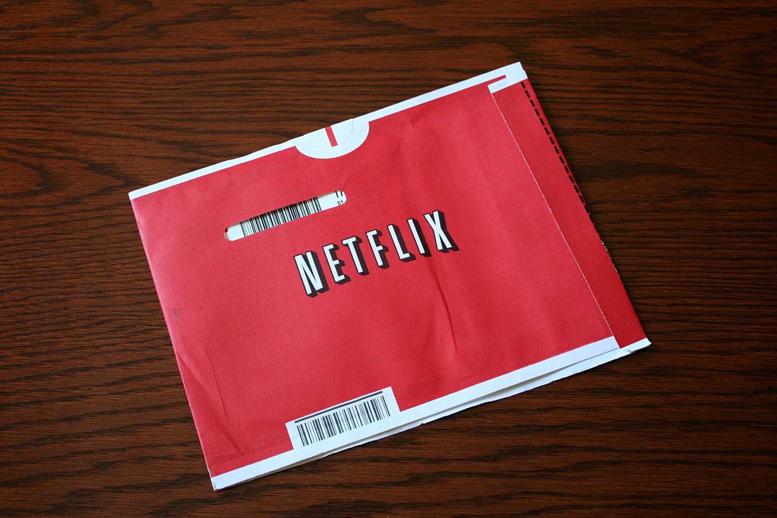A red Netflix DVD mailing envelope lying on a dark wood table