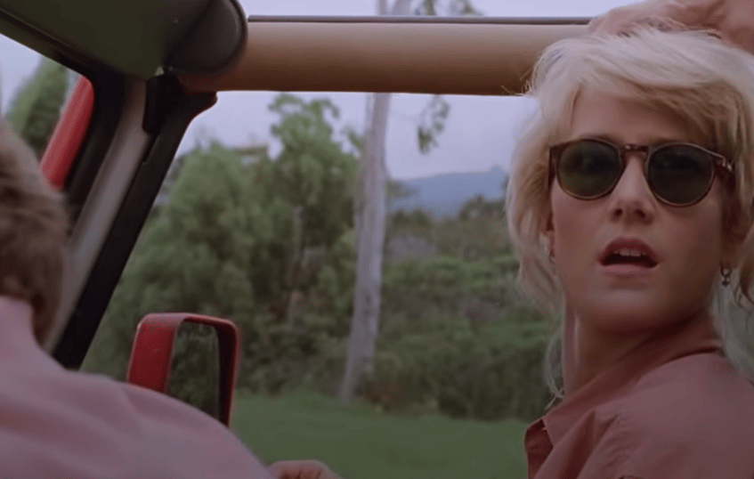 Film still of a woman in sunglasses turning to look back from the passenger seat of an open-topped jeep
