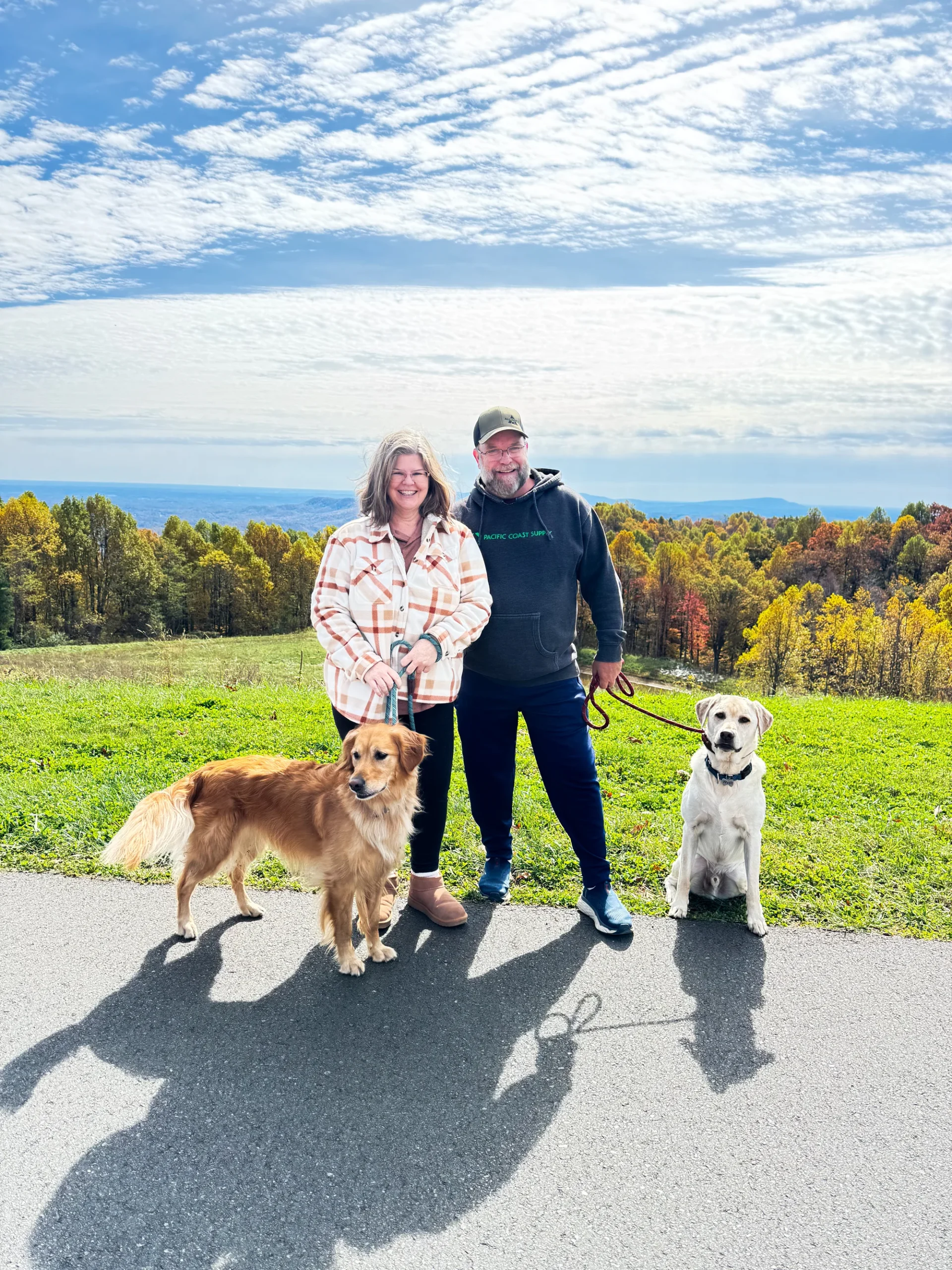 Jeannie and her husband with their two dogs on a mountain road, autumn colour across the ridge behind them